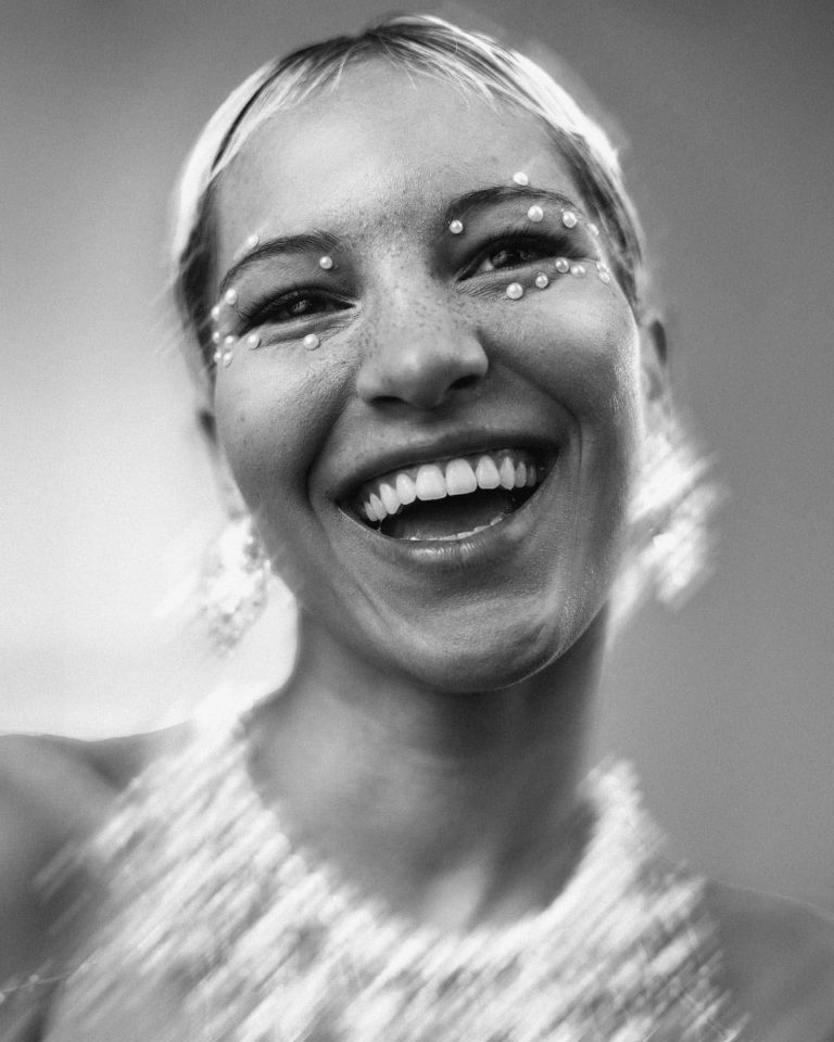 Schwarz-Weiß Foto von Frau die sich bewegt und lacht, mit weißen Perlen im Gesicht,