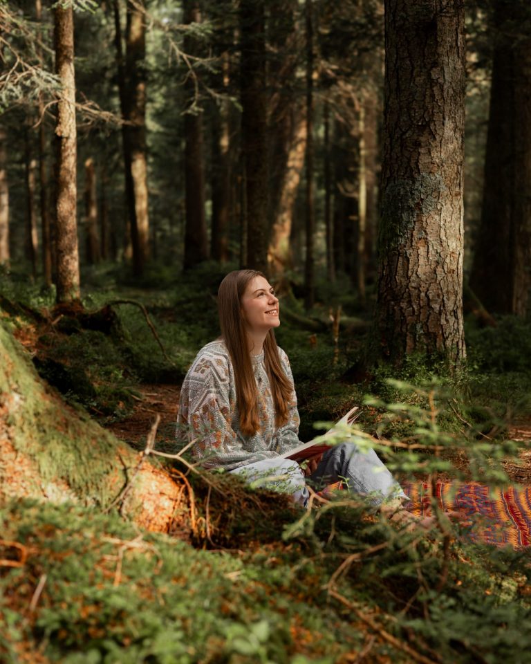 Junge Frau sitzt mit Buch im sonnigen Wald, Natur Fotoshooting Vorarlberg.