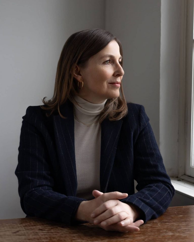 Business Portrait einer Frau im Blazer am Fenster, authentisch und professionell inszeniert.