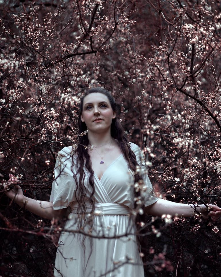 Frau im weißen Kleid umgeben von blühenden Ästen, Natur Fotoshooting Vorarlberg.