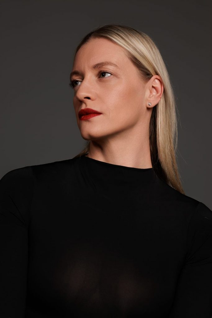 Frau mit blondem Haar und rotem Lippenstift vor grauem Hintergrund, Business Portrait Vorarlberg.