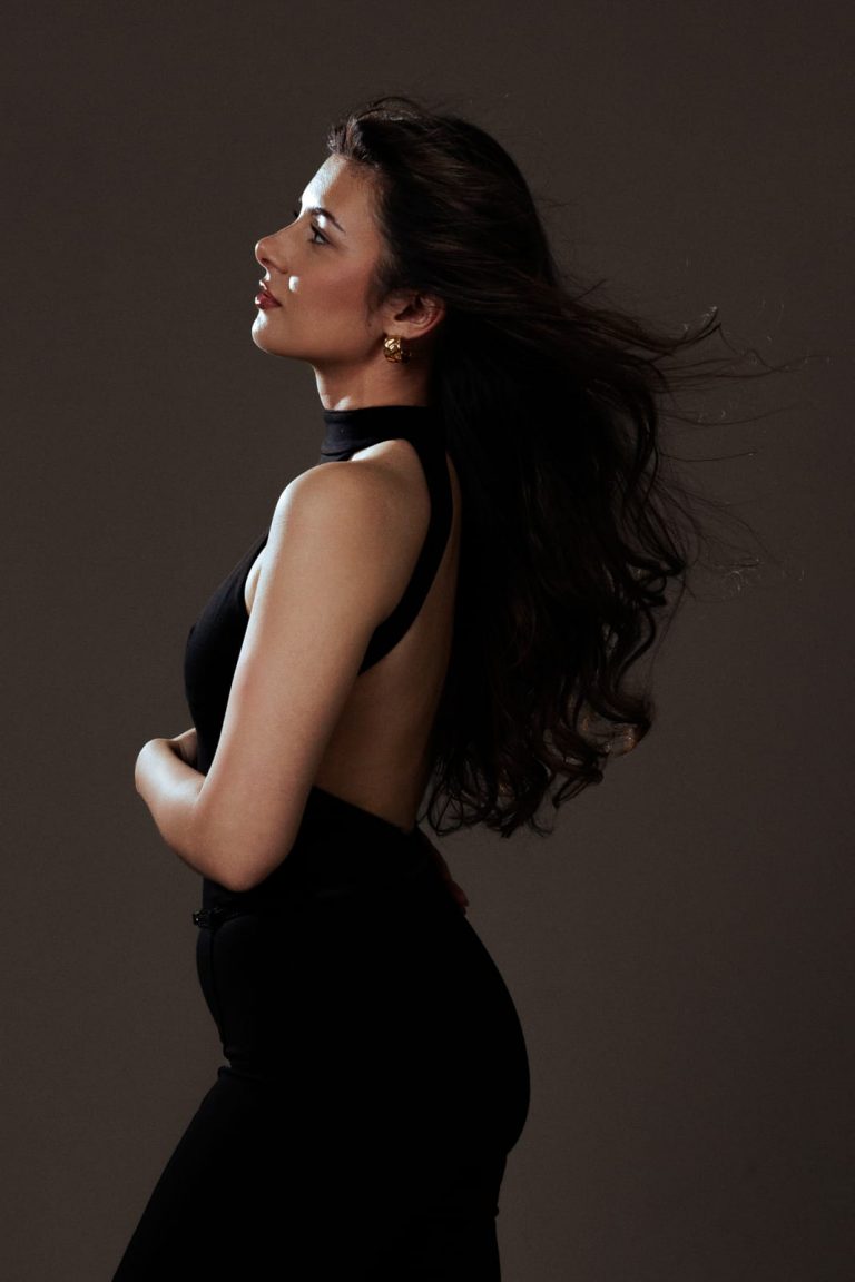 Frau im Profil mit wehendem Haar und Rückenfreiem Kleid, elegante Studioaufnahme.