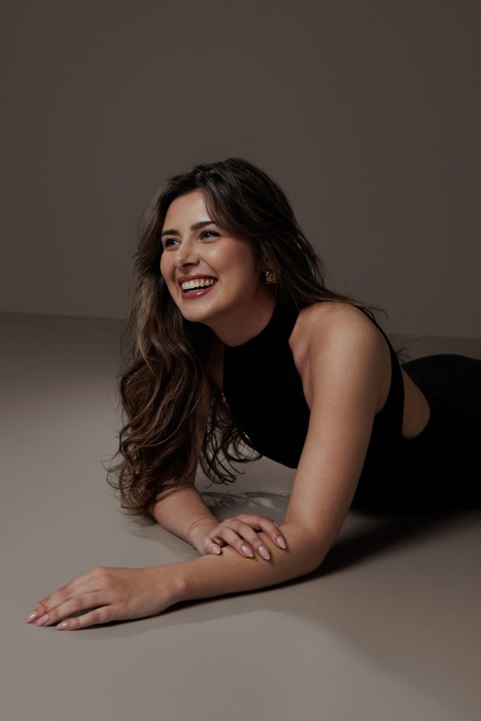 Liegend lachende Frau im schwarzen Kleid vor neutralem Hintergrund, Studio Portrait Vorarlberg.