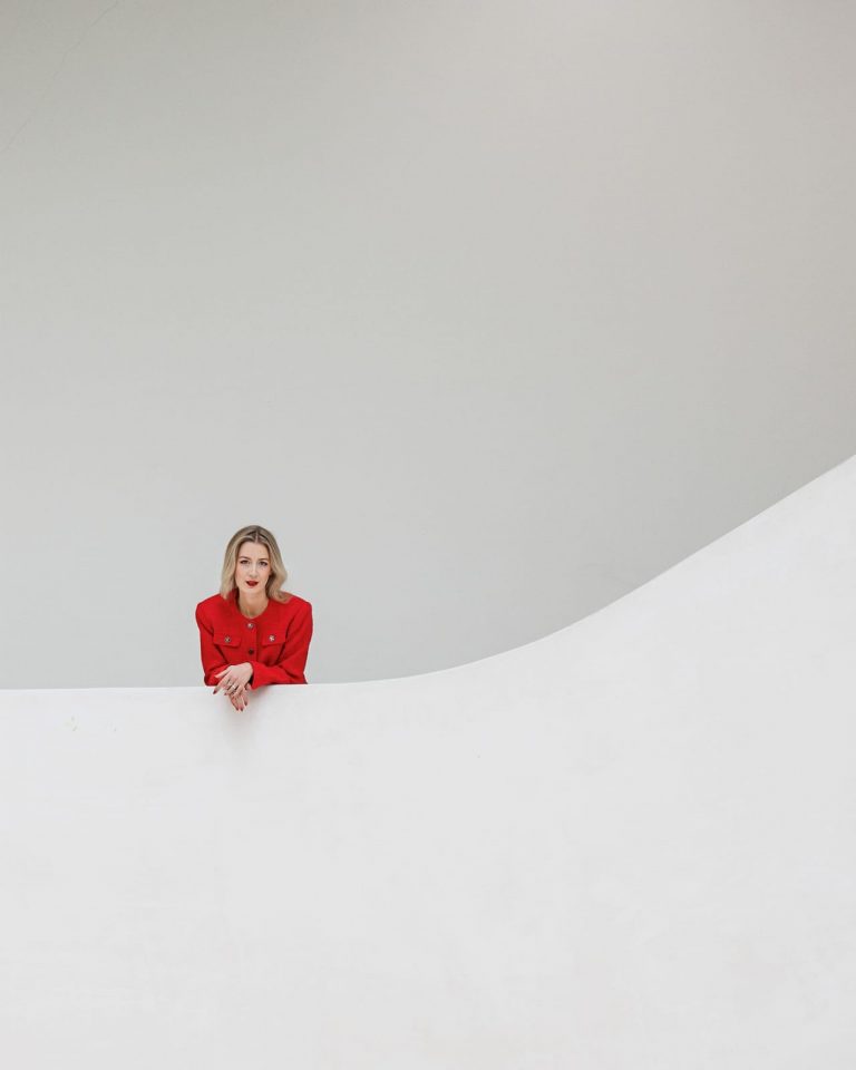 Minimalistisches Portrait einer Frau im roten Blazer vor weißer Wand, modernes Business Fotoshooting.