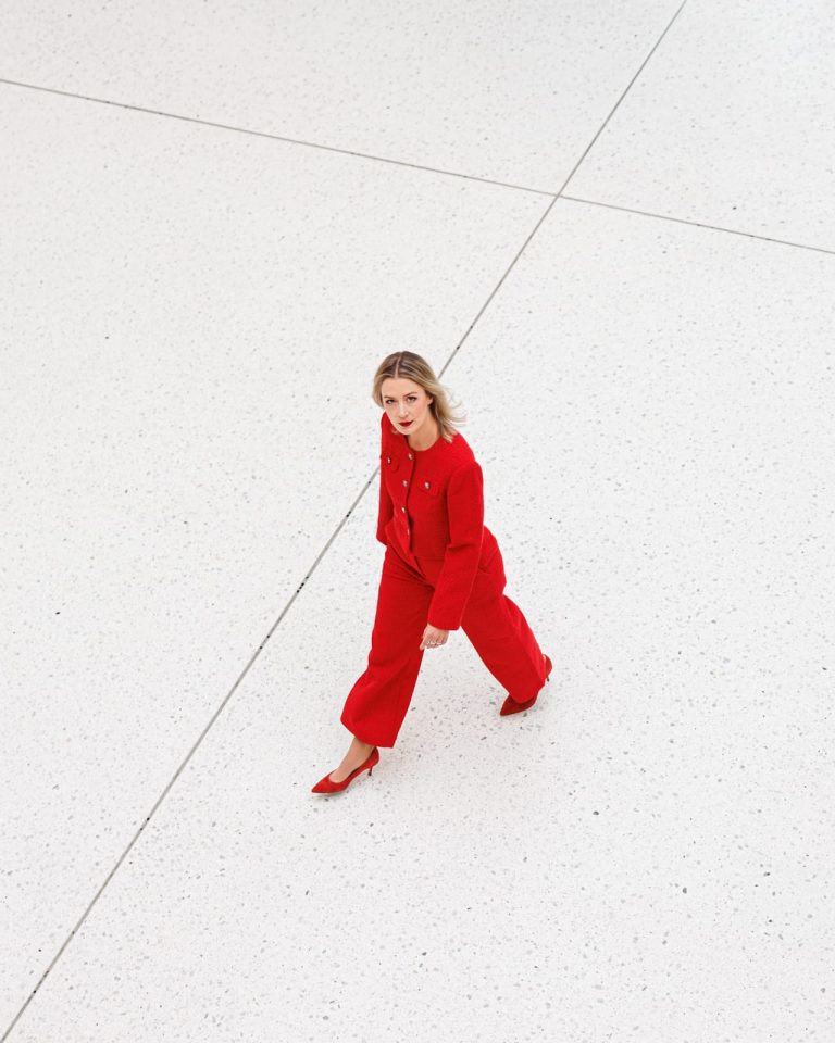 Frau im roten Hosenanzug schreitet über hellen Platz, urbanes Mode- oder Business-Fotoshooting.