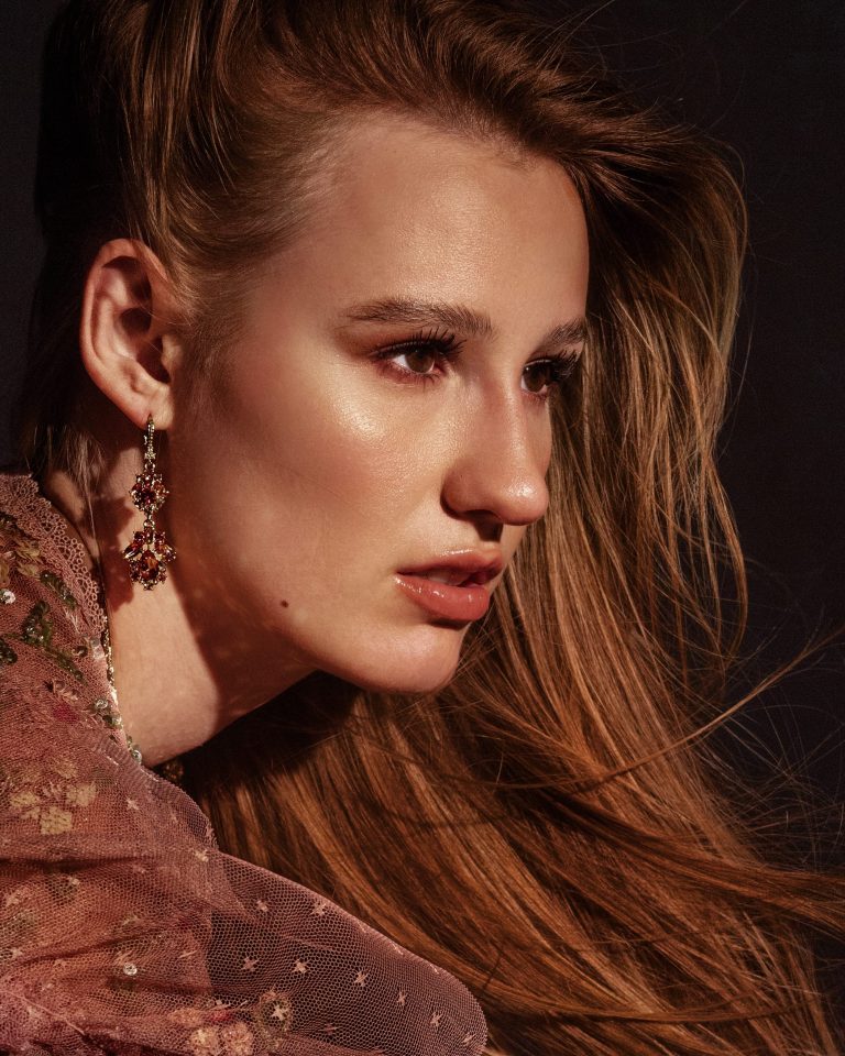 Porträt eines weiblichen Models mit glamourösem Look, weichem Licht und goldenen Statement-Ohrringen. Model Shooting, Model Fotoshooting Vorarlberg, Sedcardshooting Vorarlberg, Sedcardfotos.