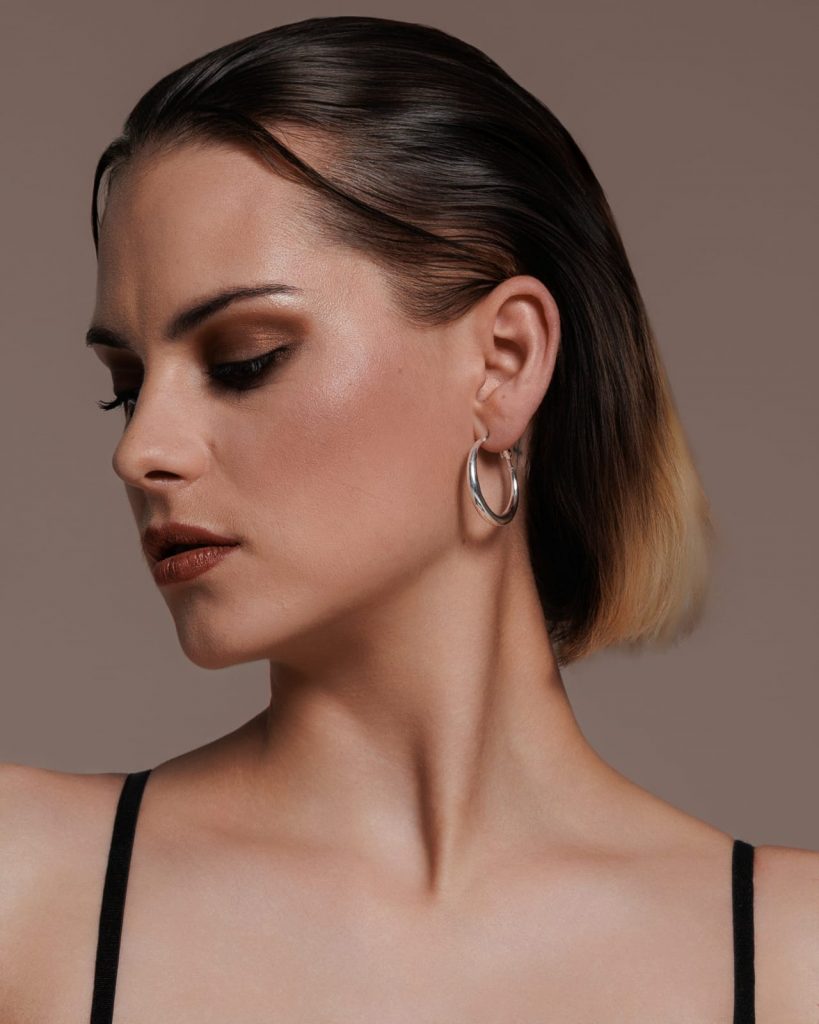 Nahaufnahme eines weiblichen Models mit sleekem Hairstyling und silbernen Creolen, betont durch starkes Make-up. Model Shooting, Model Fotoshooting Vorarlberg, Sedcardshooting Vorarlberg, Sedcardfotos.