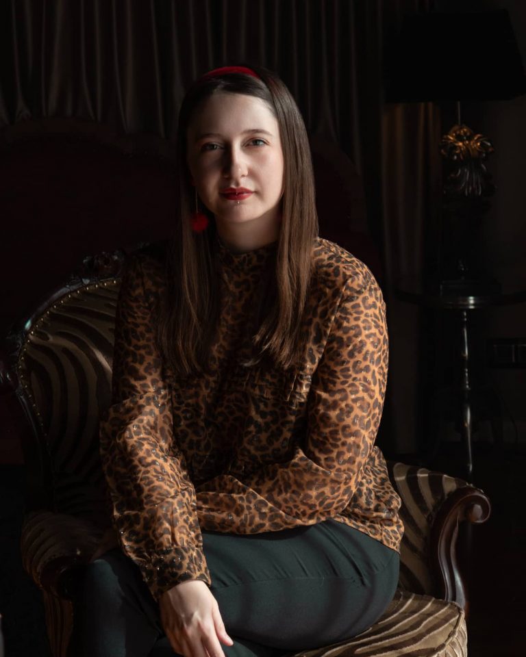 Ausdrucksstarkes Portrait von Viktoria Jäger, Fotografin in Vorarlberg, im Vintage-Ambiente auf einem gemusterten Sessel mit Leopardenbluse – spezialisiert auf persönliche und stilvolle Fotoshootings in Vorarlberg.